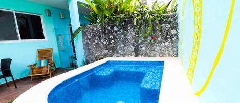 Une piscine avec un mur en pierre et des plantes, une chaise en bois et une fenêtre.