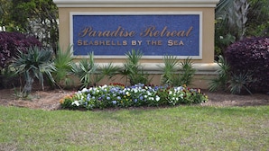 Schild für Paradise Retreat, mit einem Mosaikmuster und umgeben von einem Blumenbeet in verschiedenen Farben.
