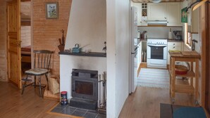 A cozy cabin interior with a fireplace, wooden walls, a dining area, and a kitchen.