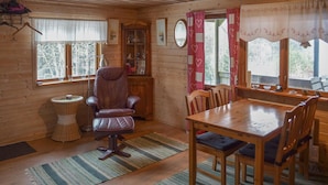 A cozy cabin interior with a dining table, chairs, a massage chair, a wicker side table, and a cabinet with glass doors.