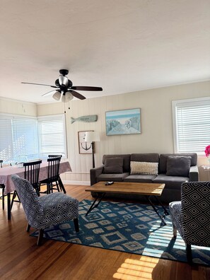 A living room with a ceiling fan, a sofa, a coffee table, patterned chairs, a rug, and a painting on the wall.