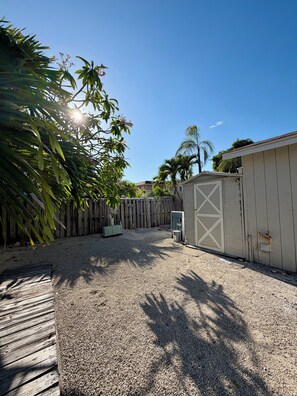 A backyard with a gravel surface, a wooden deck, a shed, and a wooden fence.