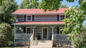 A two-story house with a red roof, a porch with white railings, and a stone foundation. - Cozy & Chic Rustic Retreat-Luxury Log Home Near Downtown, Opry and Much More (Nashville)