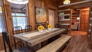 A wooden dining table with a bench, surrounded by chairs, in a room with wooden walls and a door leading to another area. - Cozy & Chic Rustic Retreat-Luxury Log Home Near Downtown, Opry and Much More (Nashville)