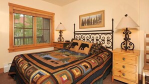 Une chambre avec une grande fenêtre, un lit recouvert d’une courtepointe, deux tables de chevet avec des lampes et un tableau accroché au mur.