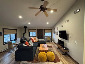 Una sala de estar moderna con un sofá modular, una mesa de centro de madera, otomanas amarillas, un televisor y una chimenea.