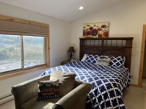 Una camera da letto con una grande finestra, un letto con copriletto decorato, una sedia con un cuscino e un quadro appeso al muro.