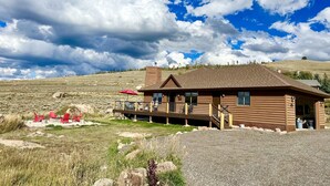 A log cabin with a deck, outdoor seating, and a view of a grassy hill. - 1 Mile to ski Area / Amazing Views / Hot Tub - Five Star Reviews (Granby)