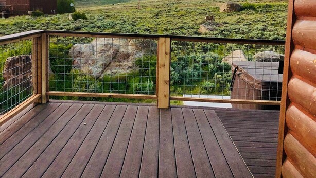 A wooden deck with a metal railing overlooking a grassy landscape with a building in the distance. - 1 Mile to ski Area / Amazing Views / Hot Tub - Five Star Reviews (Granby)