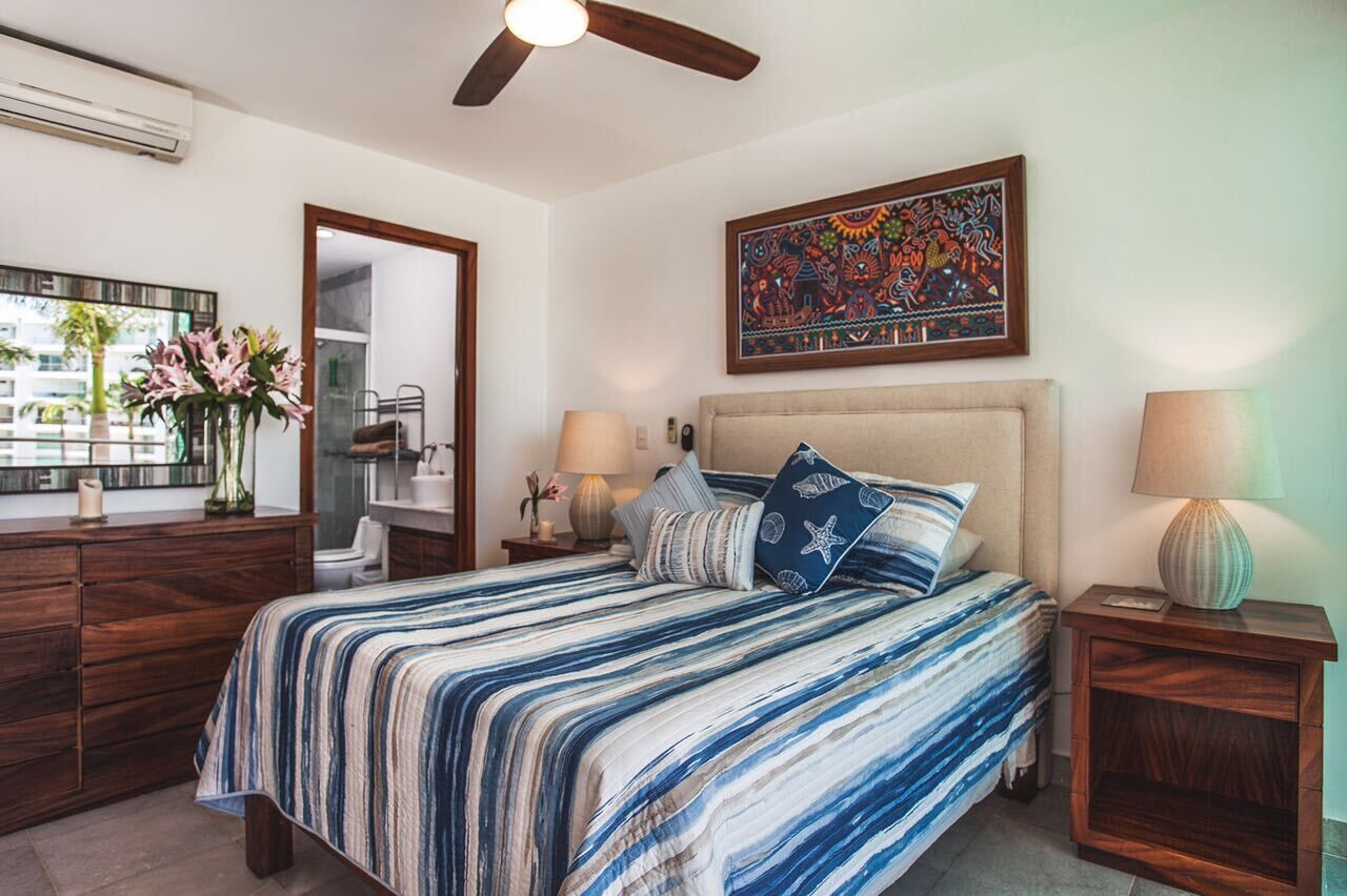 A bedroom with a bed, bedside tables, a mirror, a ceiling fan, and a wall-mounted artwork.