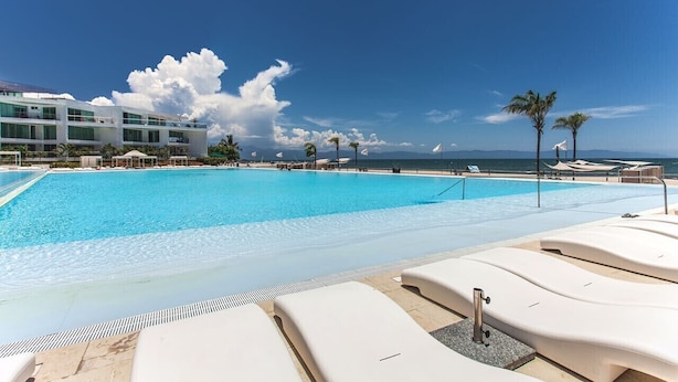 A pool area with lounge chairs, a clear sky, and a building in the background.