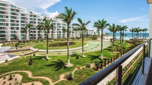A hotel with multiple floors, a landscaped garden with palm trees, and a view of the ocean.