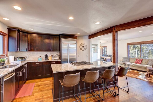 A modern kitchen with dark wood cabinets, a stainless steel refrigerator, a granite countertop, and a bar area with stools.