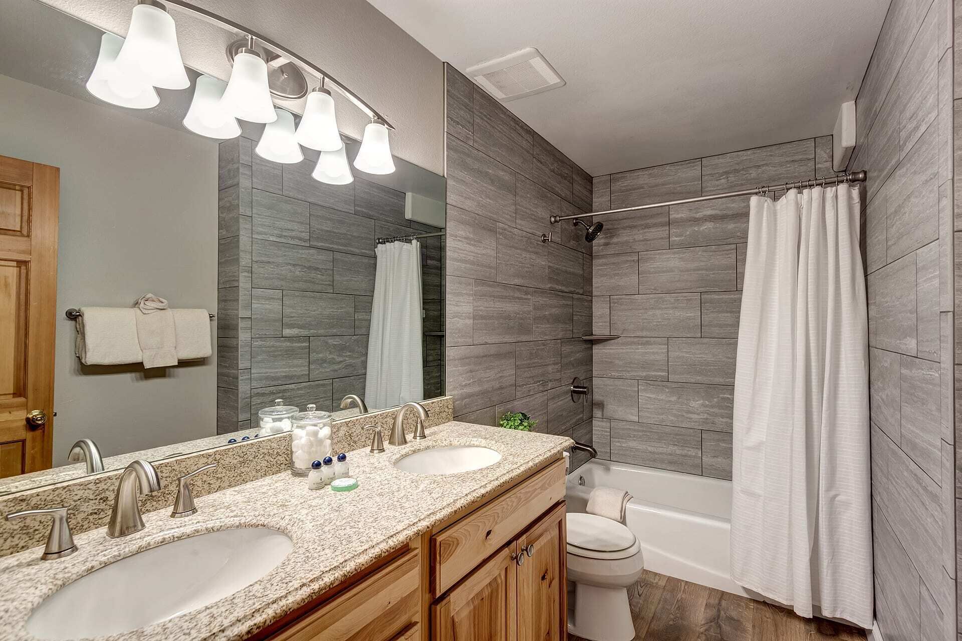 A bathroom with two sinks, a mirror, a shower, and a toilet.