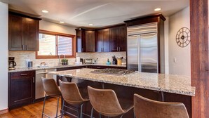 Una cocina moderna con armarios de madera oscura, un refrigerador de acero inoxidable, una isla grande con taburetes de bar y un reloj en la pared.
