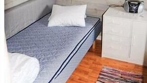 Ein kleines Zimmer mit einem Einzelbett, einem Holzkopfstück, einem Nachttisch mit Lampe und einem gerahmten Bild an der Wand.
