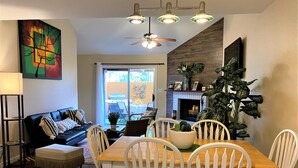 A dining area with a wooden table and white chairs, a black sofa with striped pillows, a ceiling fan, and a painting on the wall. - CΛsitΛ ΛrizonΛ - Tempe - Designed for LARGE FAMILIES + Kids (Tempe)