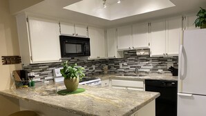 A modern kitchen with white cabinets, a black microwave, a granite countertop, and a built-in dishwasher. - CΛsitΛ ΛrizonΛ - Tempe - Designed for LARGE FAMILIES + Kids (Tempe)