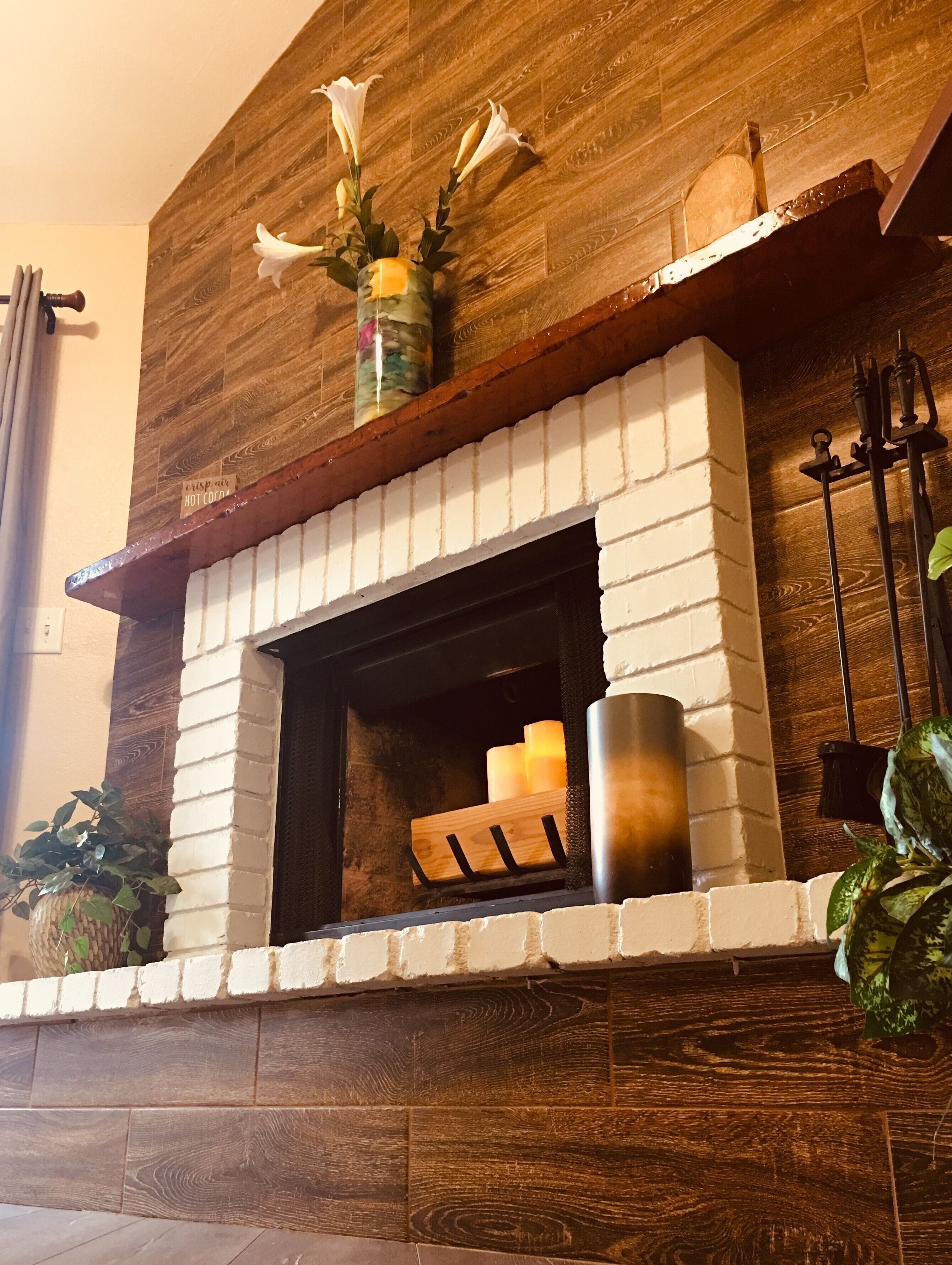 A fireplace with a brick surround, a wooden mantel, and a vase with flowers.