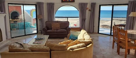 Een woonkamer met uitzicht op het strand, een bruine bank, een bijzettafeltje en een houten stoel.