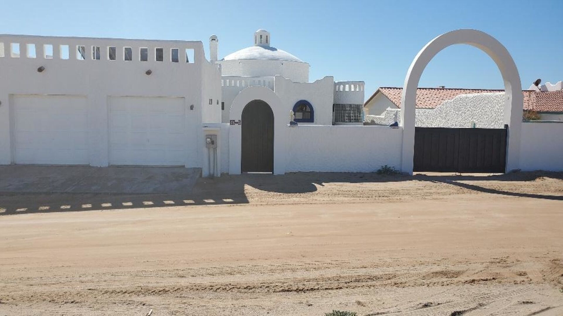 A white building with a large arched entrance, a garage, and a dome-shaped structure.