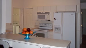 A kitchen with white cabinets, a microwave, a refrigerator, and a clock on the wall. - beautiful homeaway , 2815 sw 29th pl (Cape Coral)