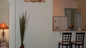 A living room with a sofa, a lamp, a vase with plants, and a kitchen area in the background. - beautiful homeaway , 2815 sw 29th pl (Cape Coral)