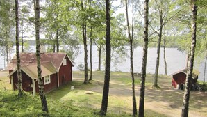 A cabin with a metal roof and a small porch, surrounded by tall trees and a lake. - 2 bedroom lovely home in Hyltebruk (Hyltebruk)