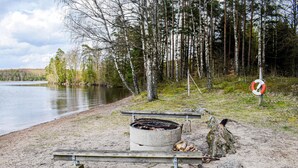 A lakeside campsite with a concrete fire pit, wooden benches, and a lifebuoy on a post. - 2 bedroom lovely home in Hyltebruk (Hyltebruk)