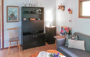 Ein Wohnzimmer mit einem Holzstuhl, einer Couch mit floralen Kissen, einer schwarzen Unterhaltungseinheit mit Regalen, einer Wandlampe und einem gerahmten Bild.