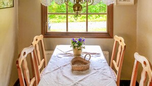Ein Esstisch mit weißer Tischdecke, einem Korbwägelchen und einer Vase mit Blumen.