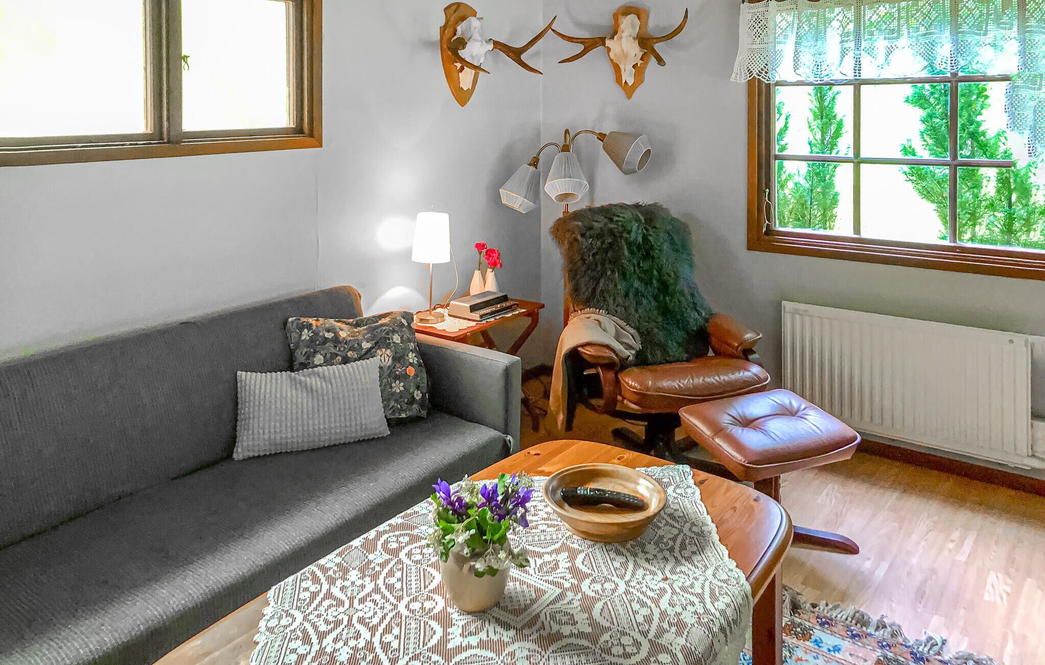 Un salon comprenant un canapé, un fauteuil, une table avec un vase et des fleurs, une lampe, et des crânes de cerf accrochés au mur.
