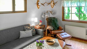 Ein Wohnzimmer mit einer Couch, einem Sessel, einem Tisch mit Schale und Blumen, einer Lampe und an der Wand befestigten Hirschskulpturen.