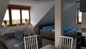 Een moderne loft slaapkamer met een schuin dak, een grijze bank, een bed met blauw beddengoed en een eethoek met een witte tafel en stoelen.