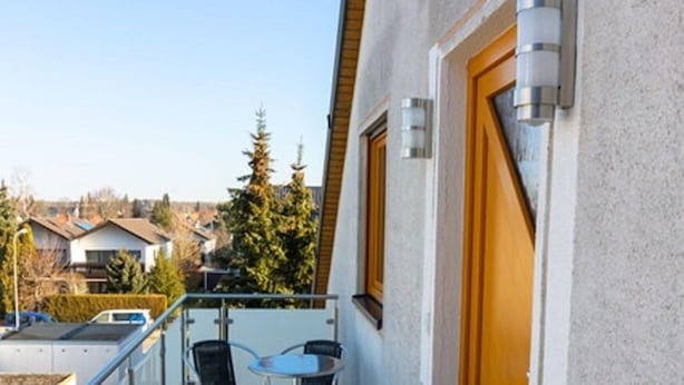 Een balkon met een tafel en stoelen, een houten deur en een uitzicht op huizen en bomen.