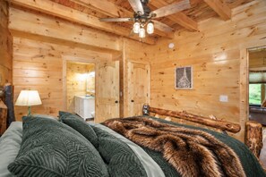 Interior de una cabaña de madera con una cama, un ventilador de techo y un cuadro en la pared.