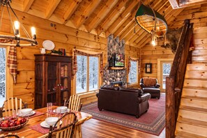 Un interior acogedor de cabaña de troncos con chimenea, muebles de madera y una zona de comedor.