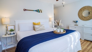 Un dormitorio ordenado con cama, mesitas de noche, lámpara de noche, espejo decorativo y un llavero de pared.