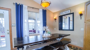 Un comedor con una mesa de madera y bancos, cortinas azules, una lámpara fijada a la pared y un letrero que dice "#Pecan Retreat".