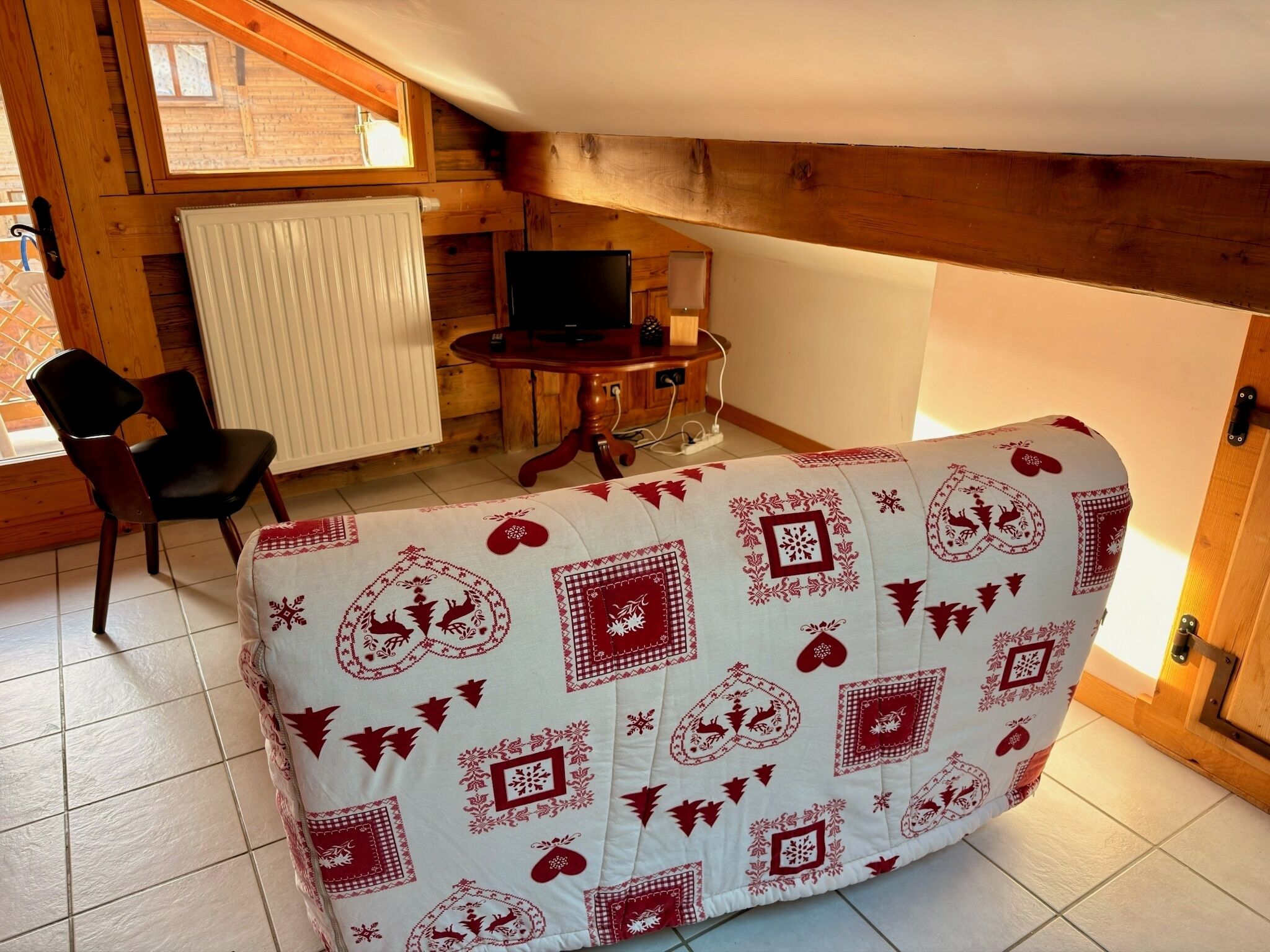 A cozy room with a patterned sofa, a wooden table with a TV, a chair, and a radiator.