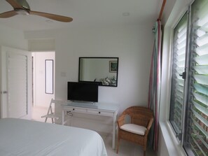 A bedroom with a bed, a desk, a chair, a television, and a window with blinds.