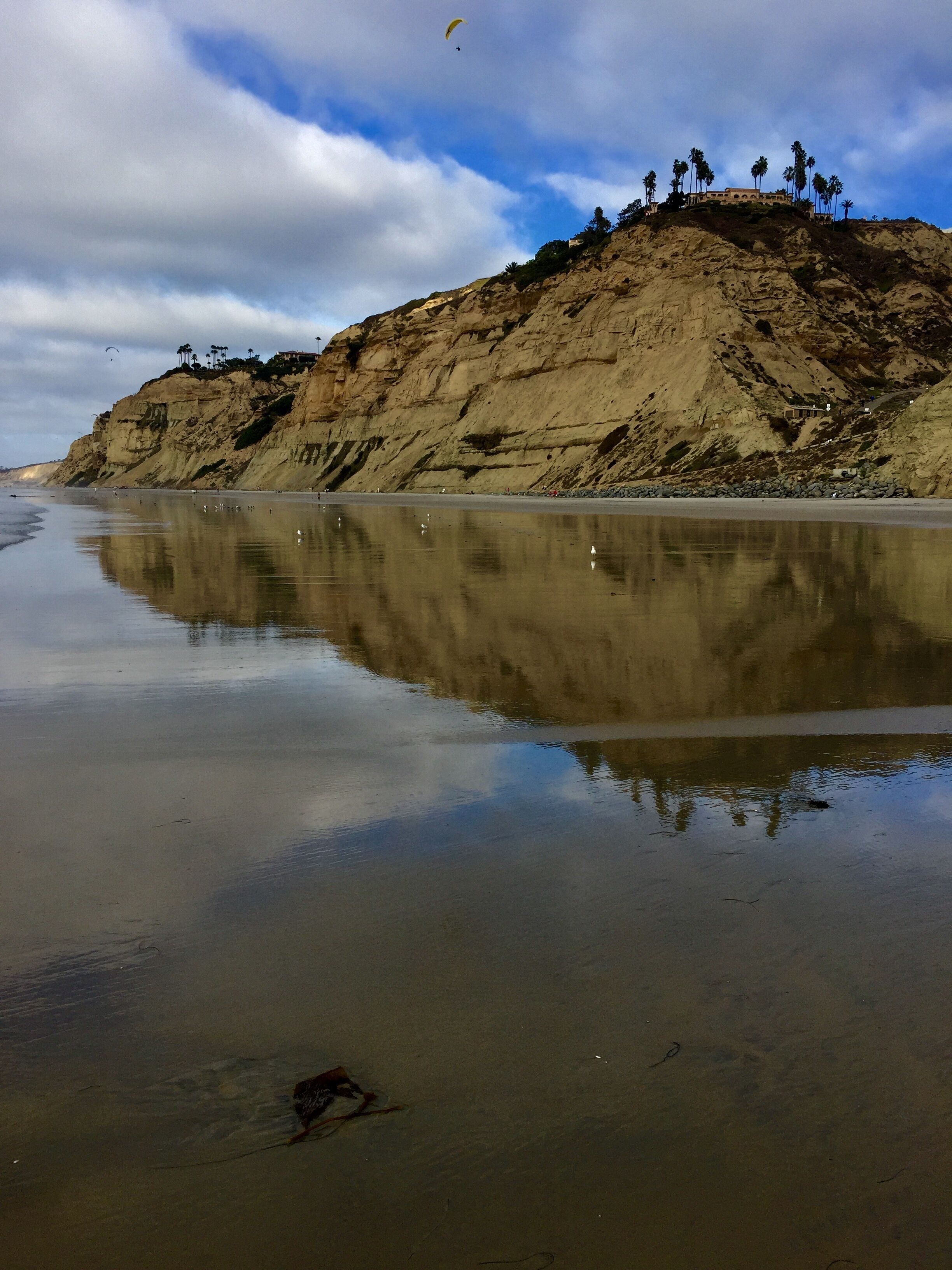 A beach with a rocky cliff and a clear reflection in the water.