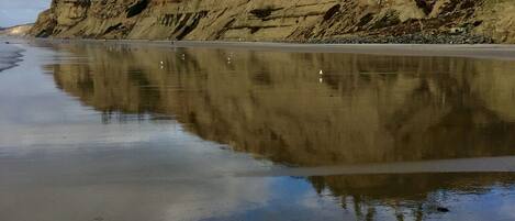 A beach with a rocky cliff and a clear reflection in the water.