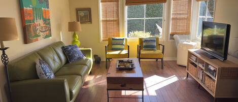 A living room with a green sofa, two yellow armchairs, a coffee table, a TV on a wooden stand, and a painting on the wall.