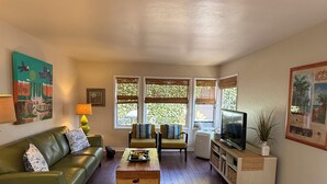 A living room with a green sofa, two armchairs, a coffee table, a TV stand, and a painting on the wall. - La Jolla Shores Beach Cottage (La Jolla)