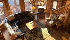 A log cabin interior with a leather sofa, armchairs, a chandelier, and a wooden staircase. - Majestic Mountaintop Retreat- Breathtaking Views, Luxury Lodge over Pigeon Forge (Sevierville)