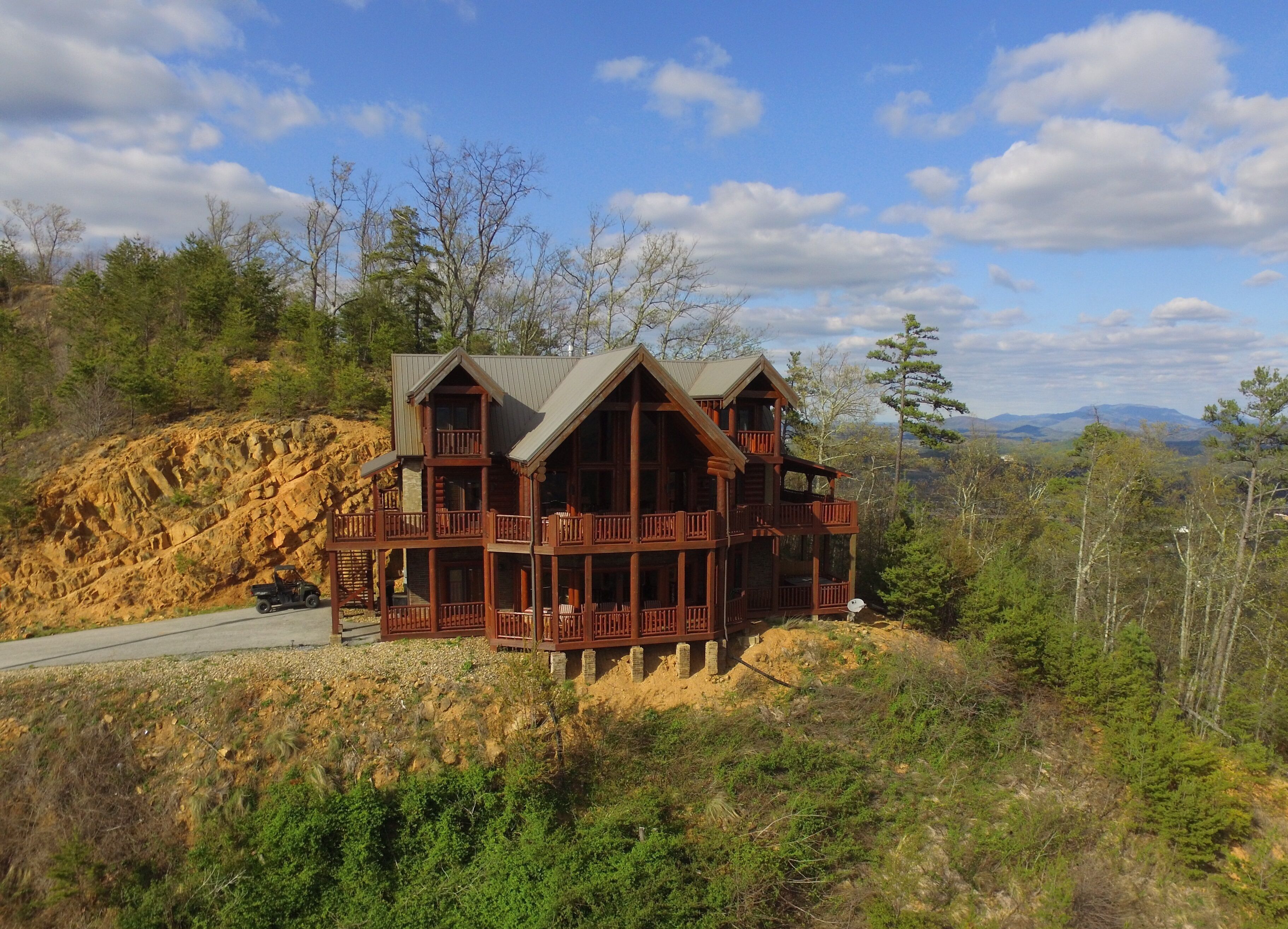 Une grande cabane en bois dotée de nombreux balcons, située sur une colline et offrant une vue sur les montagnes lointaines.