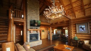 A log cabin interior with a fireplace, wooden furniture, a chandelier, and a television. - Majestic Mountaintop Retreat- Breathtaking Views, Luxury Lodge over Pigeon Forge (Sevierville)