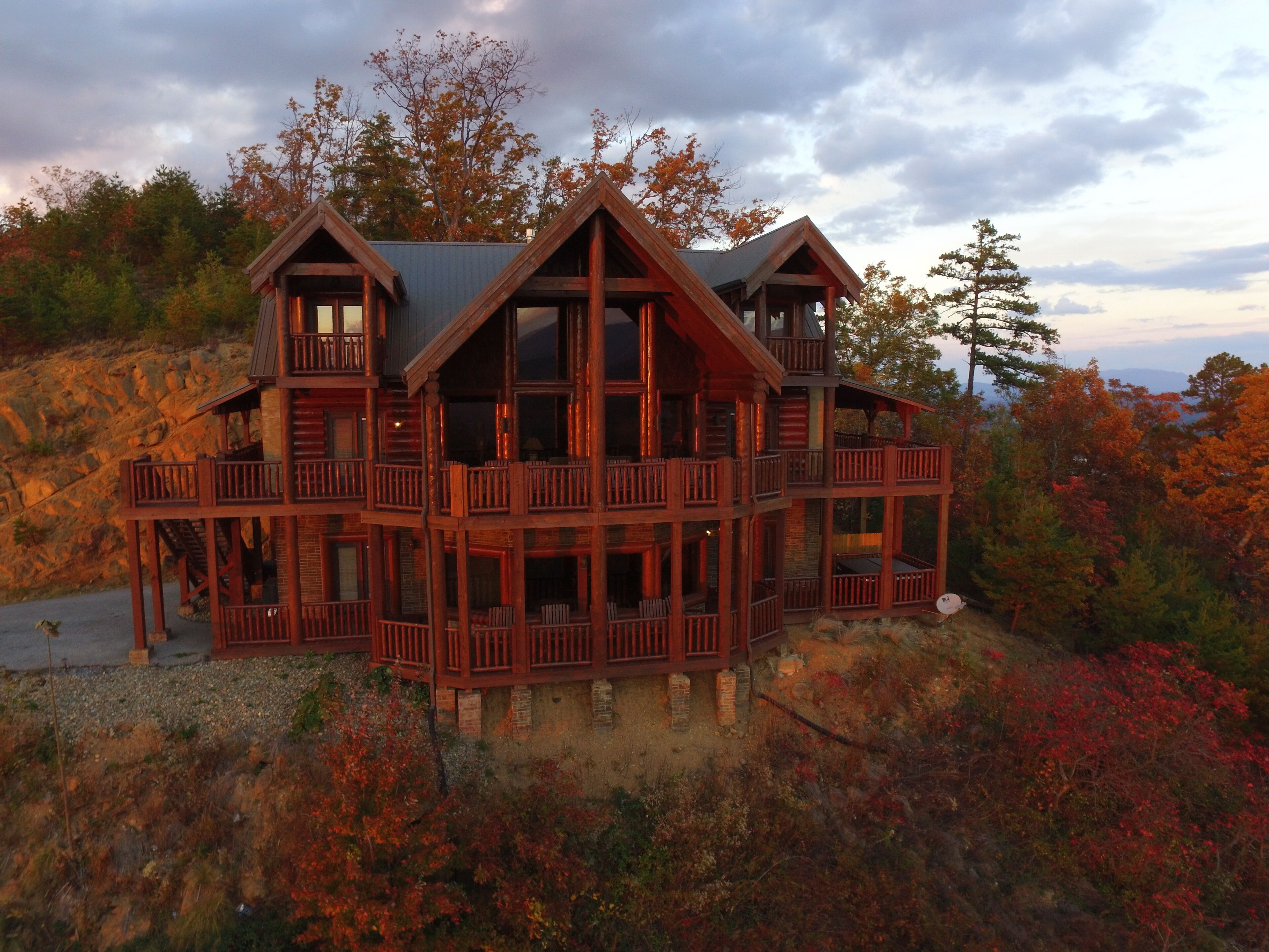A multi-story wooden cabin with balconies, situated on a hillside with autumn foliage.