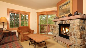 A cozy living room with a stone fireplace, a sofa, a coffee table, and large windows. - Mountain Condo for 4 | Hot Tub + Pool Access (Dillon)